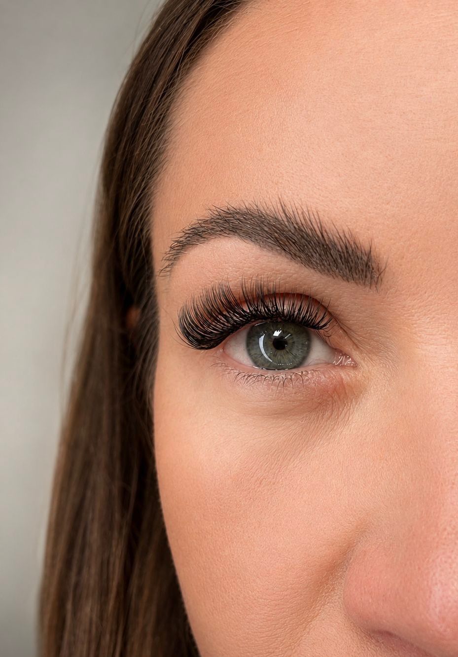 Close-up of a person's eye with long, dark eyelashes against a neutral background