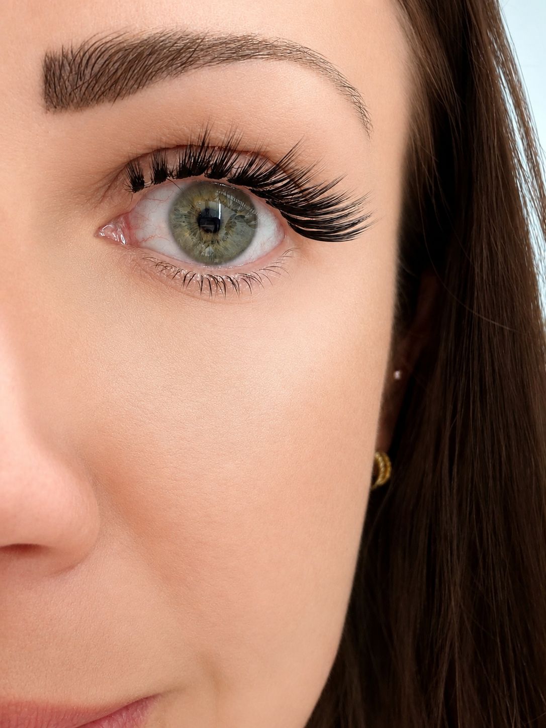 Close-up of a woman's eye with long eyelashes and a gold earring.