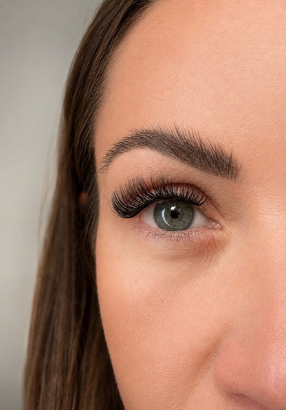 Close-up of a person's eye with long, dark eyelashes against a neutral background