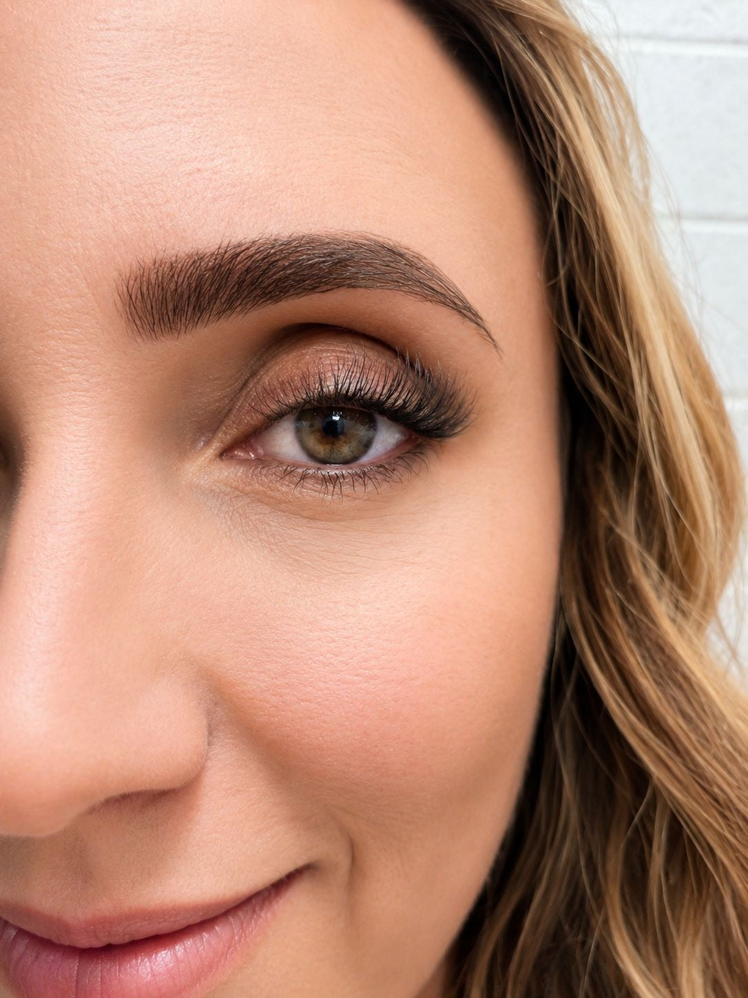 Close-up of a woman's face with a neutral expression, showing her eyelashes and part of her hair.